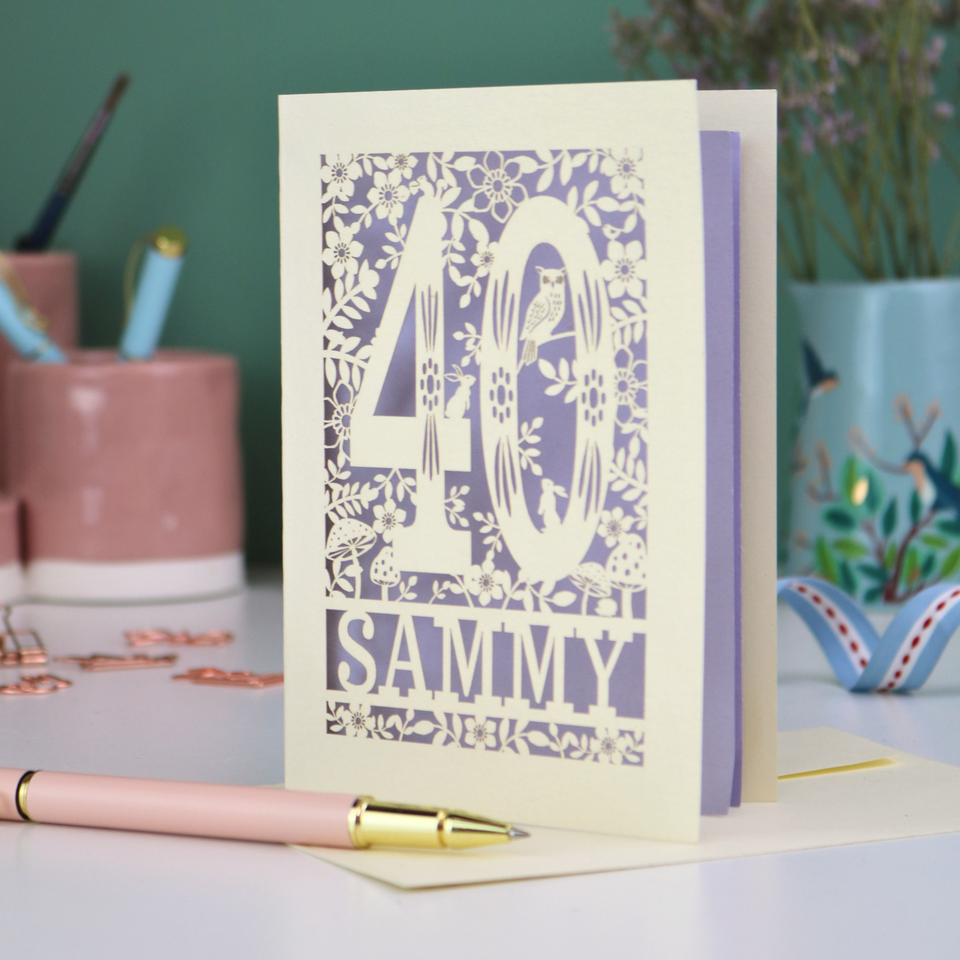 A laser cut 40th birthday card with woodland design, decorative number '40 and personalised with a name, 'Sammy', on a white desk with pen and stationery items