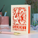A laser cut 40th birthday card with woodland design, decorative number '40 and personalised with a name, 'Sammy', on a white desk with pen and stationery items