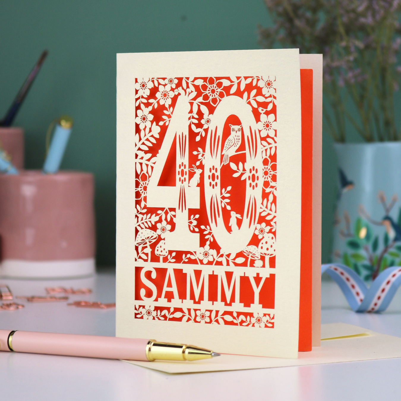 A laser cut 40th birthday card with woodland design, decorative number '40 and personalised with a name, 'Sammy', on a white desk with pen and stationery items