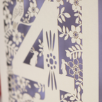 Decorative 4th Birthday card with woodland laser cut patterns, personalised with the name 'Harley', on a table with stationery items.
