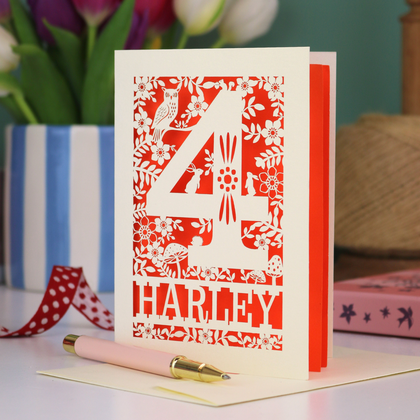 Decorative 4th Birthday card with woodland laser cut patterns, personalised with the name 'Harley', on a table with stationery items.