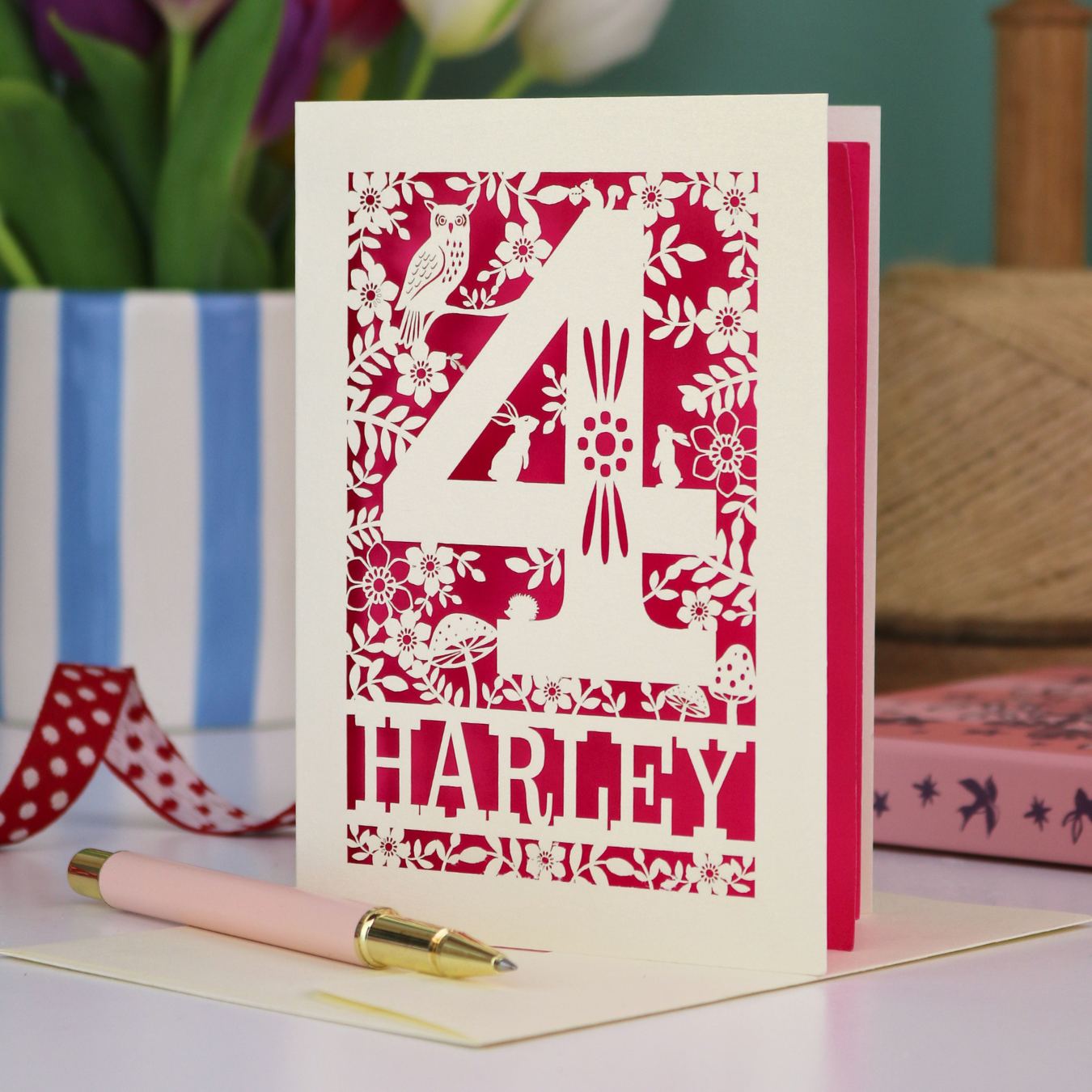 Decorative 4th Birthday card with woodland laser cut patterns, personalised with the name 'Harley', on a table with stationery items.