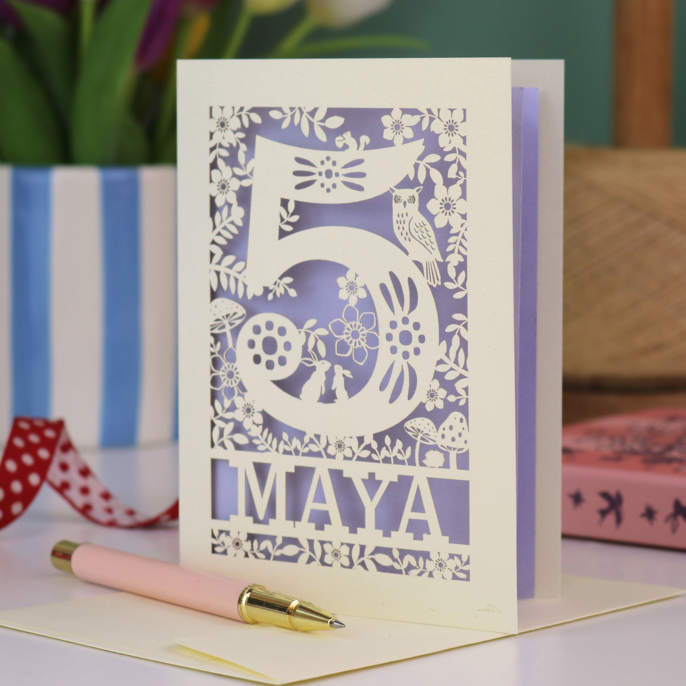 Decorative child's 5th birthday card with '5 MAYA' and woodland laser cut design on a table with flowers and books in the background