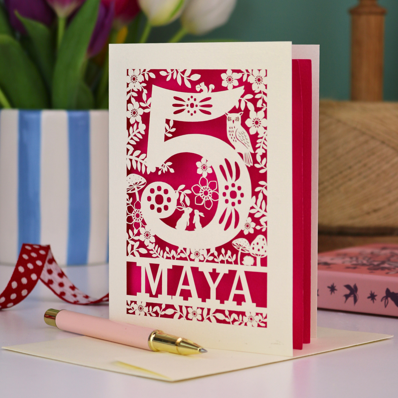 Decorative child's 5th birthday card with '5 MAYA' and woodland laser cut design on a table with flowers and books in the background