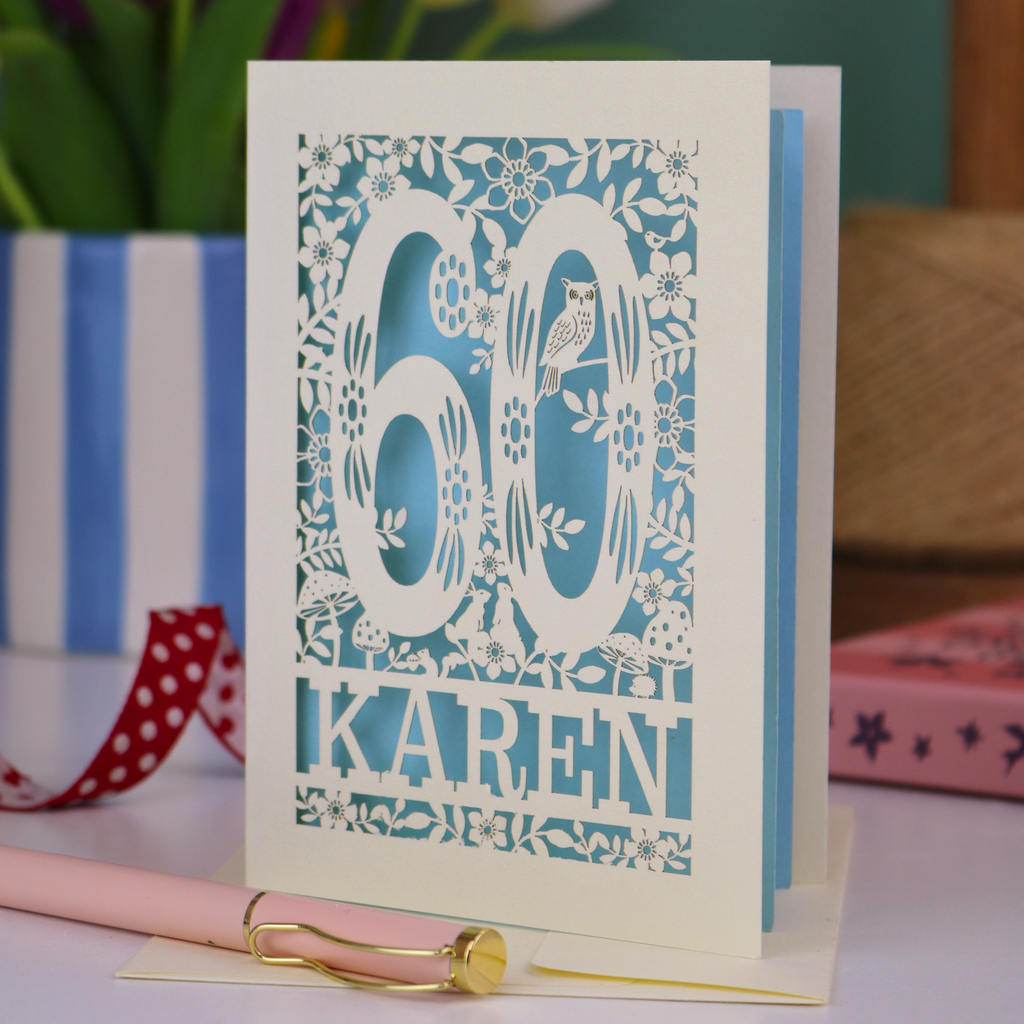 60th birthday card with floral design and 'KAREN' text on a table with stationery items.