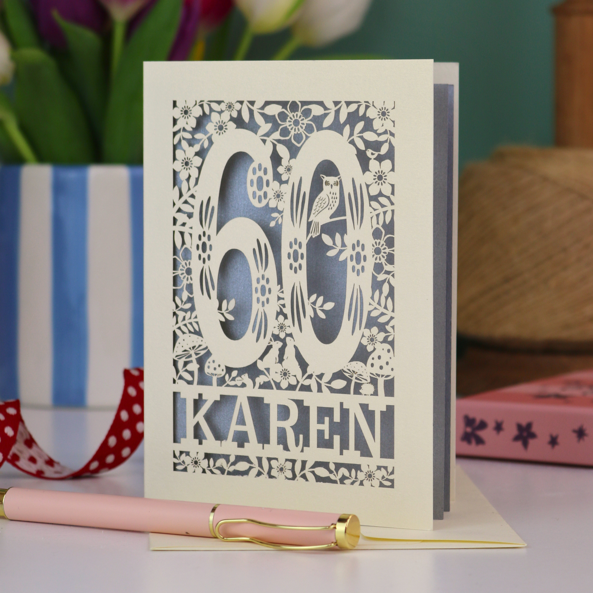 Cut out 60th birthday card with '60 Karen' design on a table with flowers and pen in the background