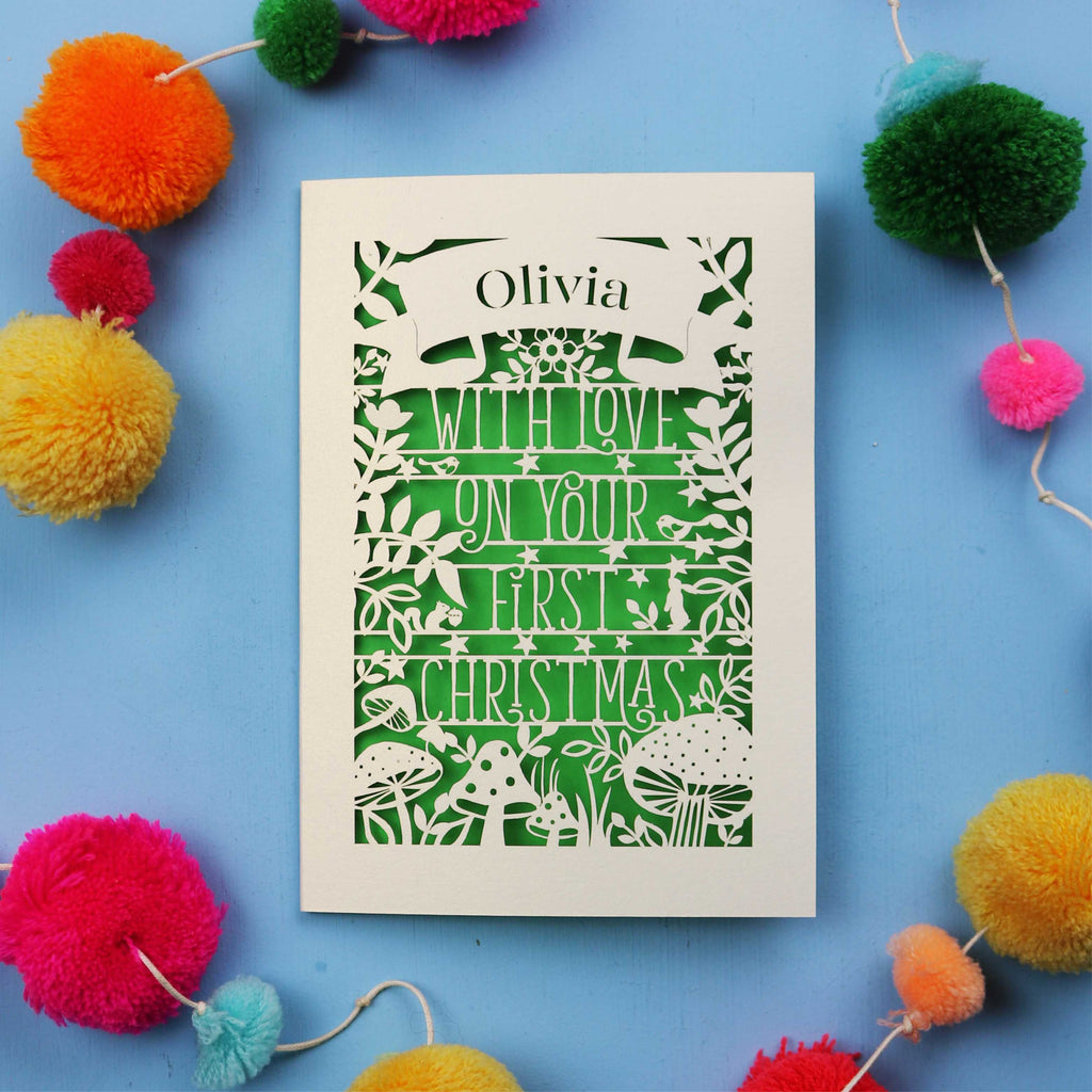 Baby's first Christmas Card with 'Olivia with love on your first Christmas' text surrounded by colourful pom-poms on a blue background