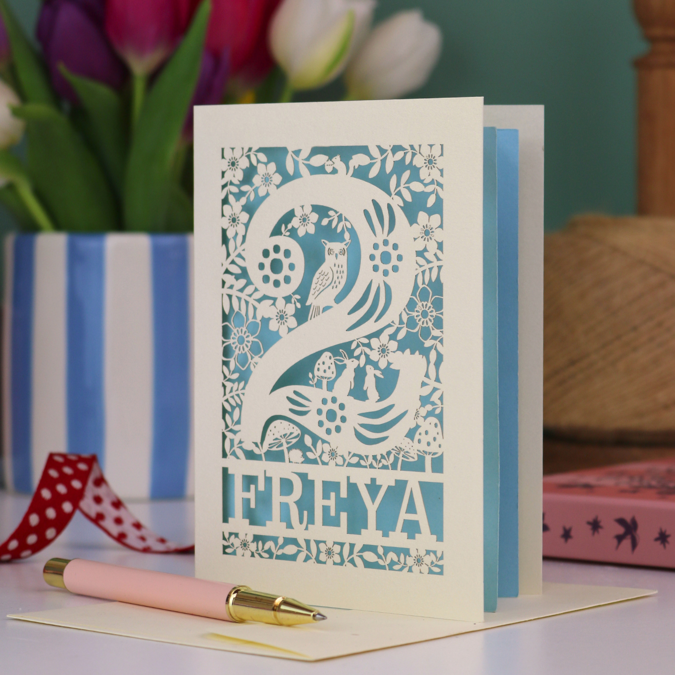 A laser cut 2nd birthday card with woodland design and decorative '2', personalised with a name. The card has tiny cut out woodland elements including bunnies, toadstools, squirrel and owl.