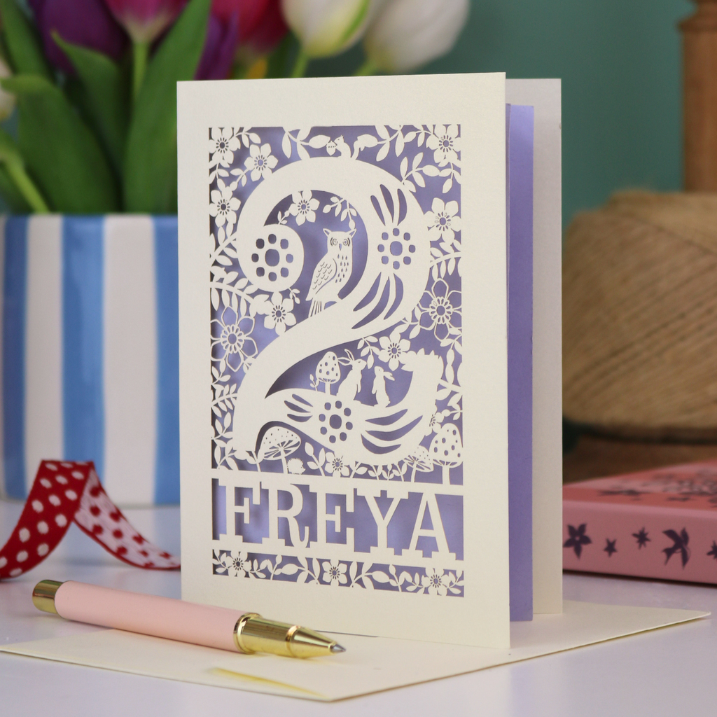 A laser cut 2nd birthday card with woodland design and decorative '2', personalised with a name. The card has tiny cut out woodland elements including bunnies, toadstools, squirrel and owl.