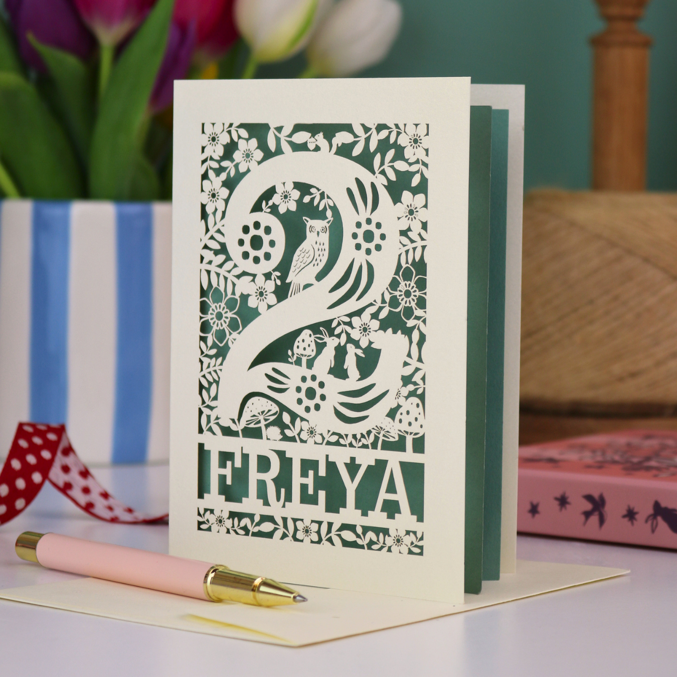 A laser cut 2nd birthday card with woodland design and decorative '2', personalised with a name. The card has tiny cut out woodland elements including bunnies, toadstools, squirrel and owl.