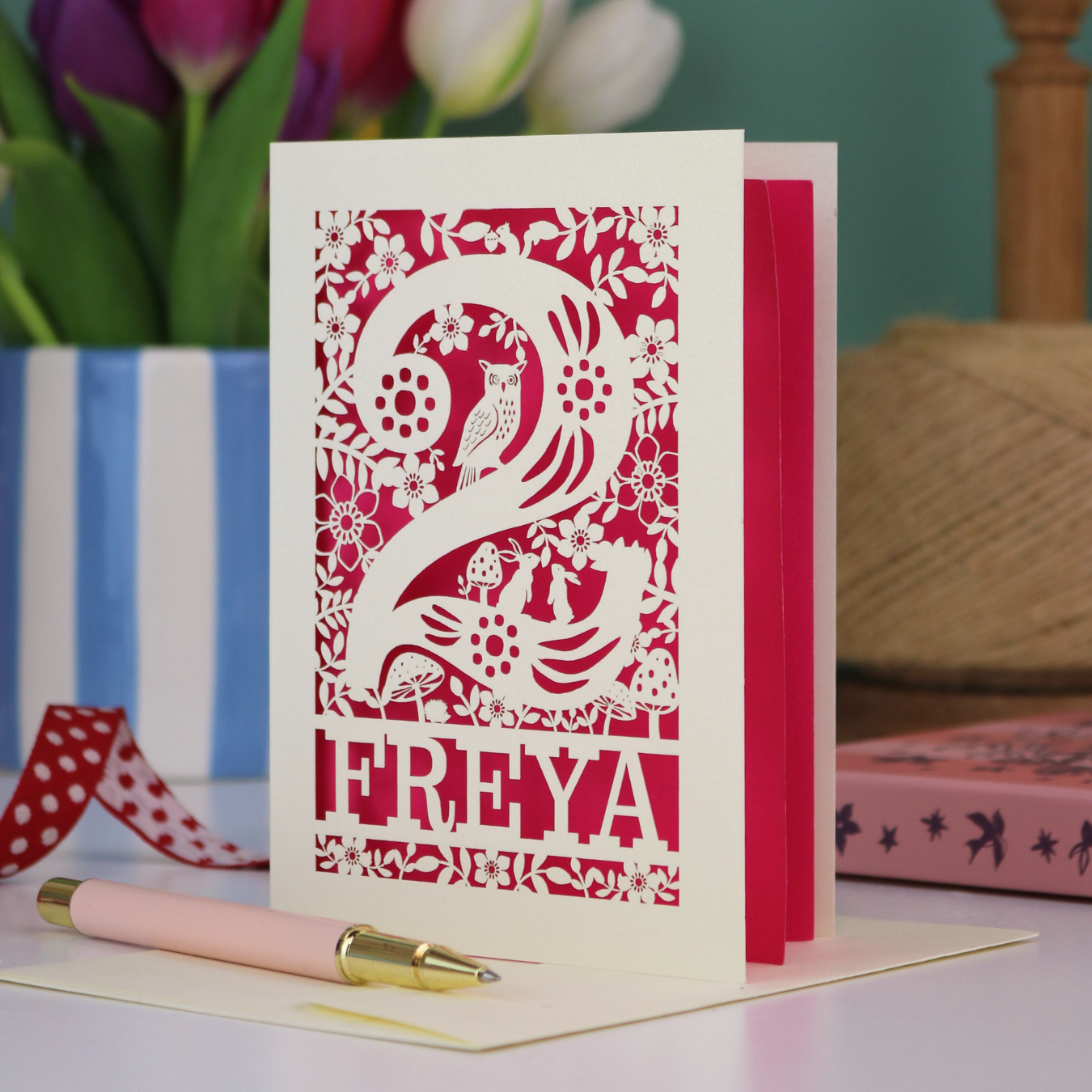 A laser cut 2nd birthday card with woodland design and decorative '2', personalised with a name. The card has tiny cut out woodland elements including bunnies, toadstools, squirrel and owl.