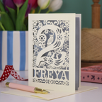 A laser cut 2nd birthday card with woodland design and decorative '2', personalised with a name. The card has tiny cut out woodland elements including bunnies, toadstools, squirrel and owl.