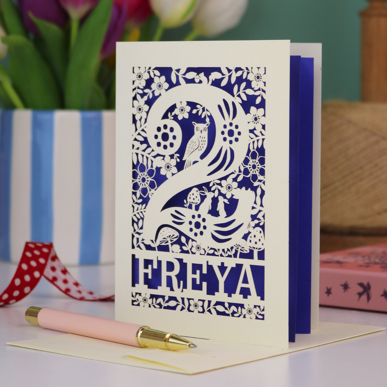 A laser cut 2nd birthday card with woodland design and decorative '2', personalised with a name. The card has tiny cut out woodland elements including bunnies, toadstools, squirrel and owl.