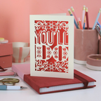 A laser cut funny Valentines card that says "You'll Do" on desk with pink background