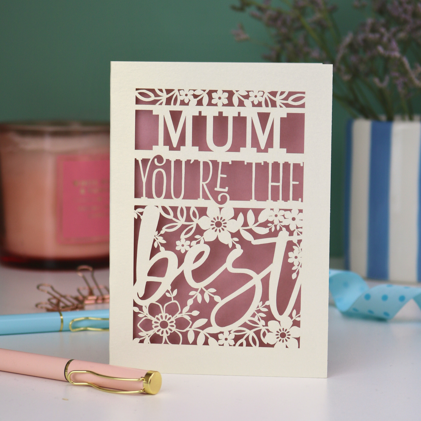 A laser cut Mother's Day card that says 'Mum, You're the best', with floral design elements. Card stands on a white desk with stationery items