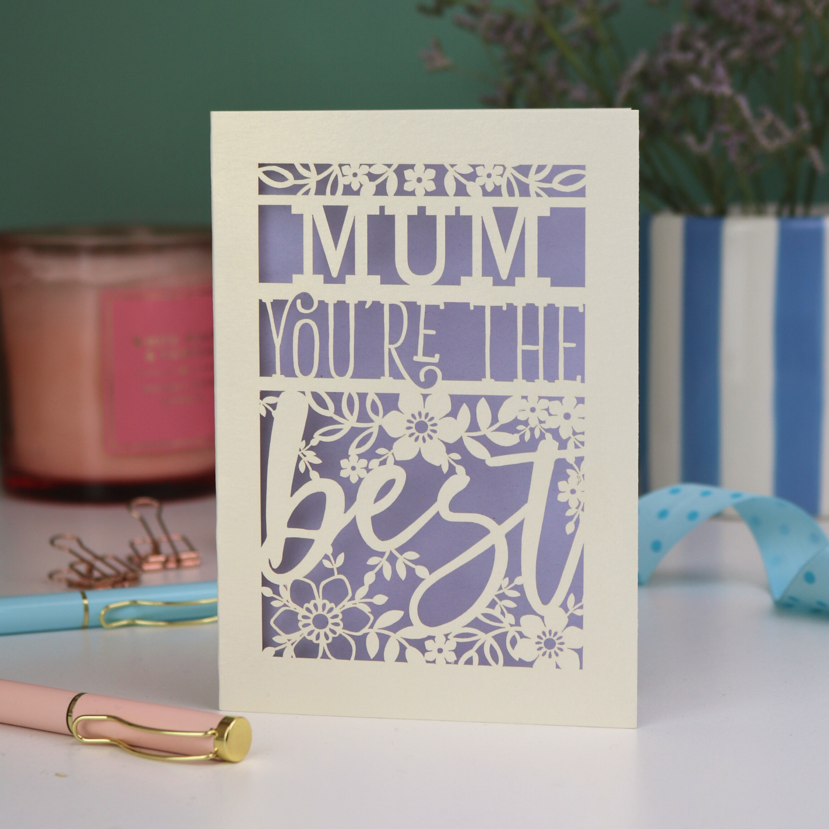 A laser cut Mother's Day card that says 'Mum, You're the best', with floral design elements. Card stands on a white desk with stationery items