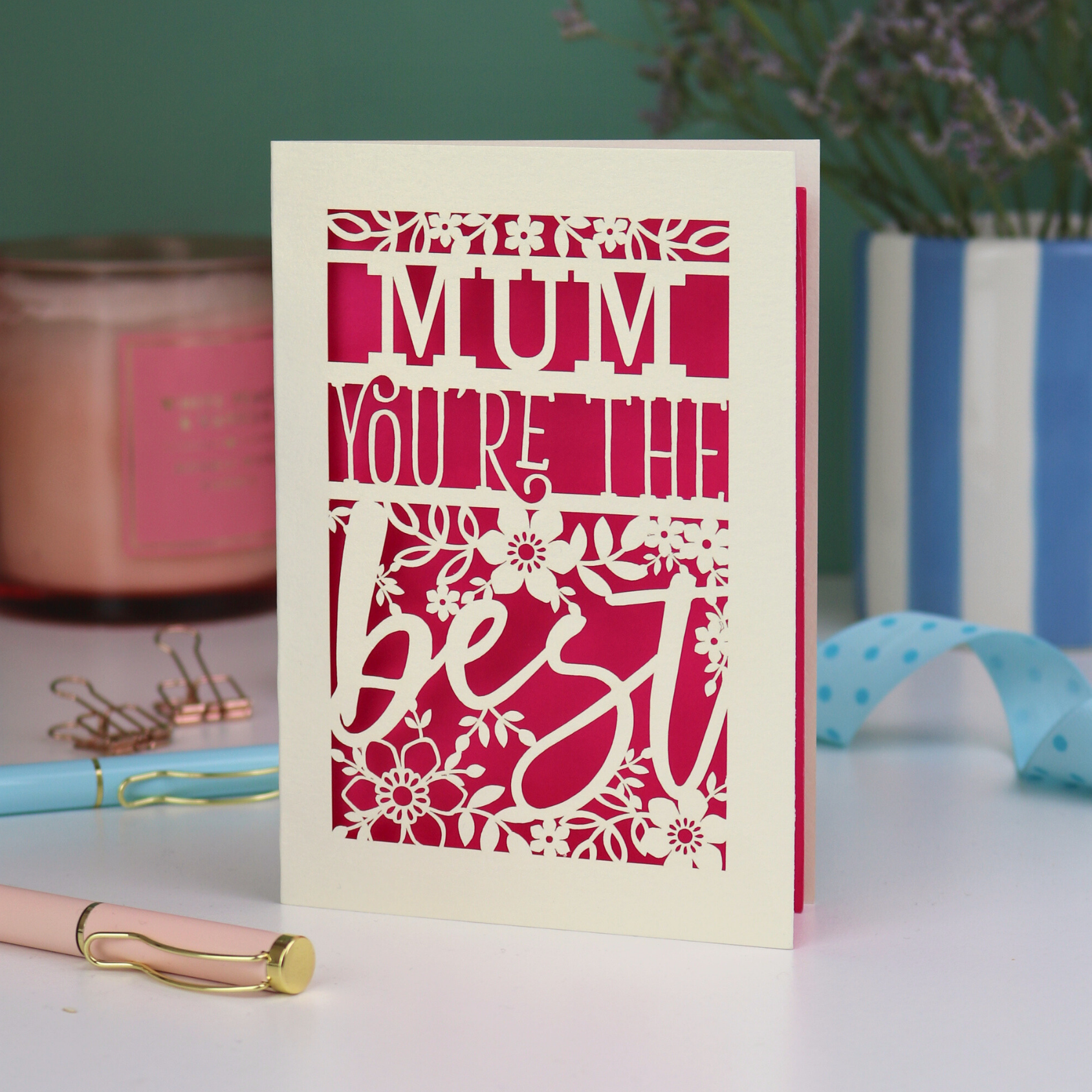 A laser cut Mother's Day card that says 'Mum, You're the best', with floral design elements. Card stands on a white desk with stationery items