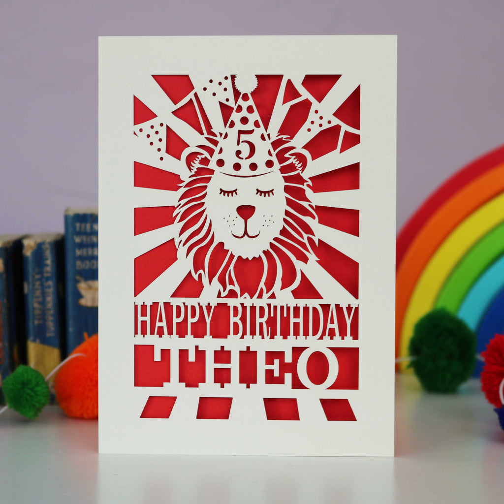A laser cut lion birthday card, personalised with a name and age and featuring a lion in a party hat