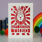 A laser cut lion birthday card, personalised with a name and age and featuring a lion in a party hat