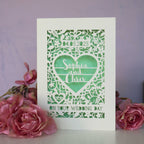 Laser cut wedding cards, cut from cream card with a light green paper insert behind.  Card features floral shapes around a heart with the names "Sophia & Chris". The date is in a banner at the top, and a line of text at the bottom reads "On Your Wedding Day."