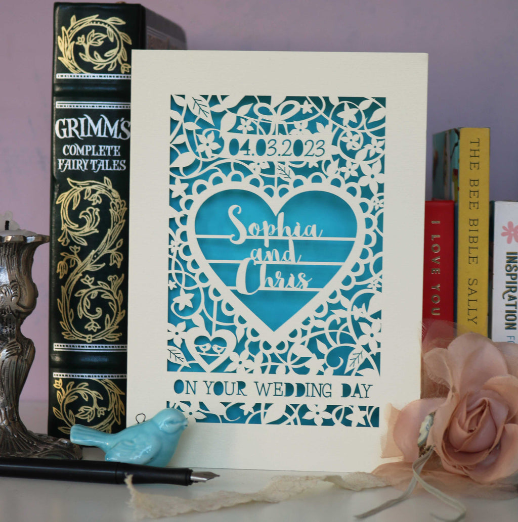 A laser cut wedding card personalised with names and date. This one is cream and blue and is intricately laser cut with flowers and leaves, a big heart, names and date of wedding. 
