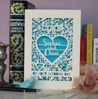 A laser cut wedding card personalised with names and date. This one is cream and blue and is intricately laser cut with flowers and leaves, a big heart, names and date of wedding. 