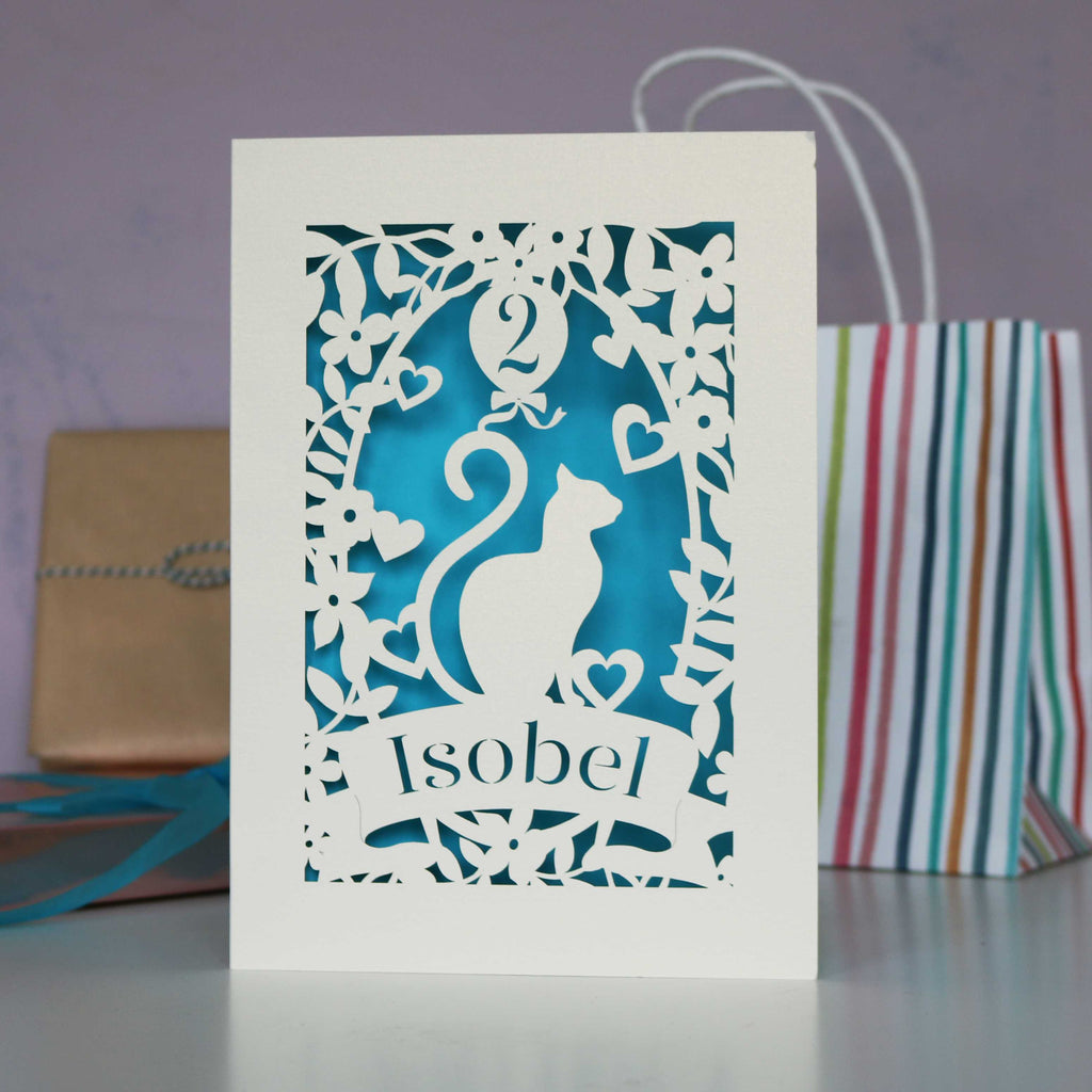 Cat design laser cut birthday card for the cat lovers in your life. Shown  cut from cream card with a peacock blue insert. Personalise with their name in the banner and their age in the balloon.