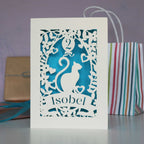 Cat design laser cut birthday card for the cat lovers in your life. Shown  cut from cream card with a peacock blue insert. Personalise with their name in the banner and their age in the balloon.