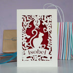 Elegant cat design papercut card. Personalised with a name in the banner and an age in the balloon. Laser cut from cream card with a dark red background.