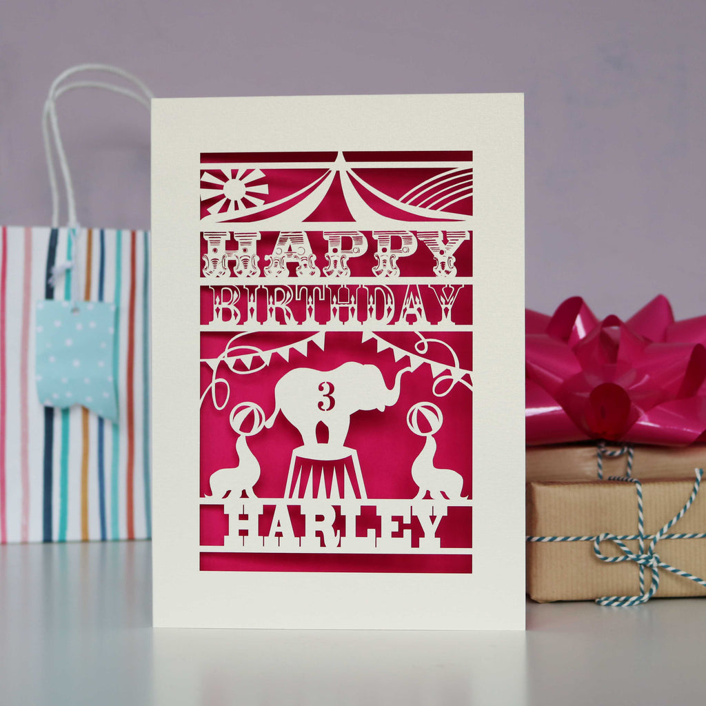 Circus themed Big Top card showing an elephant and seals performing un the Big Top. Personalised with age and name and laser cut from cream card with a bright pink background.