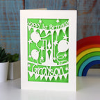 A cream and green paper cut first birthday card for grandson or granddaughter. Card is personalised with a name.
