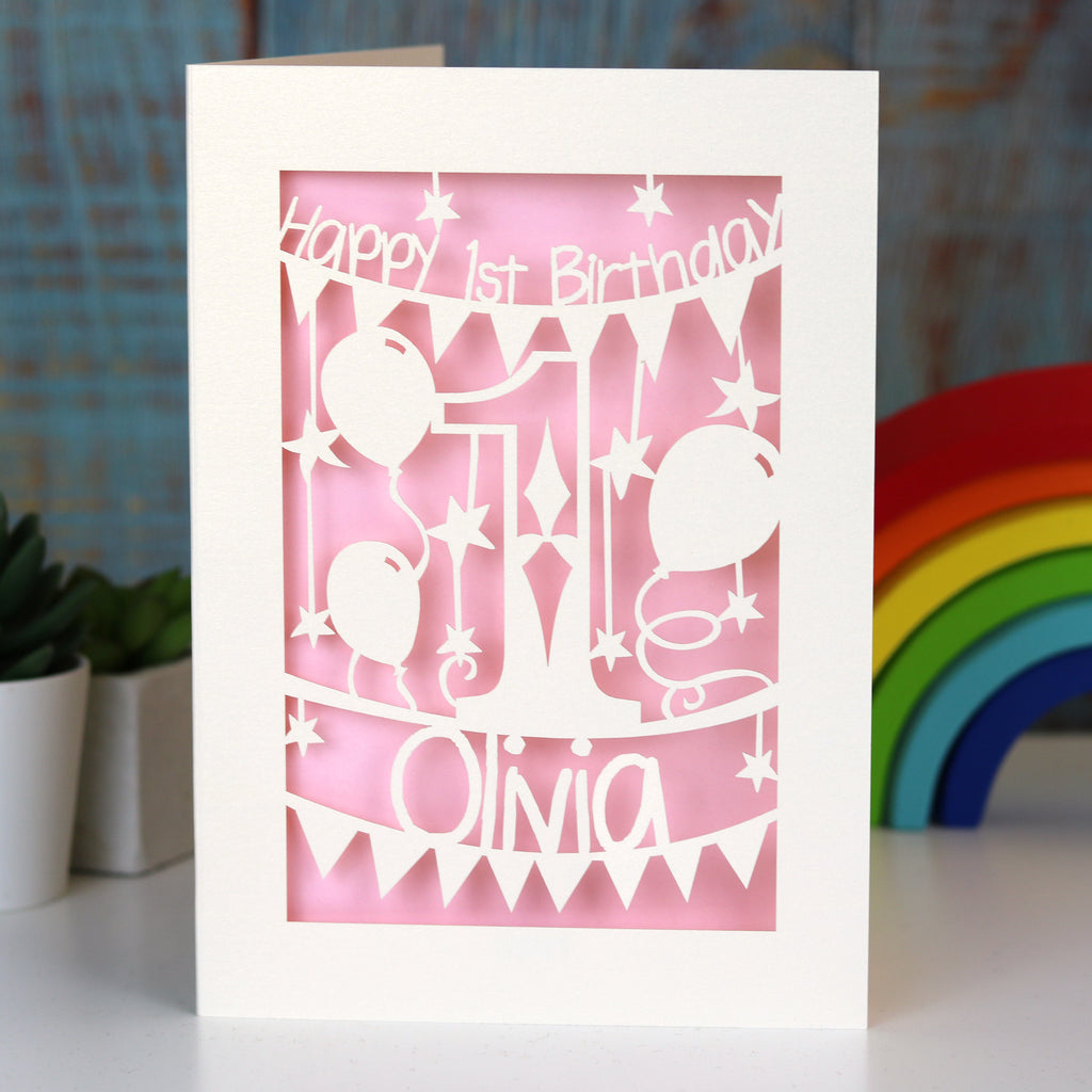A laser cut card for a first birthday. This card is cream with a candy pink paper behind.