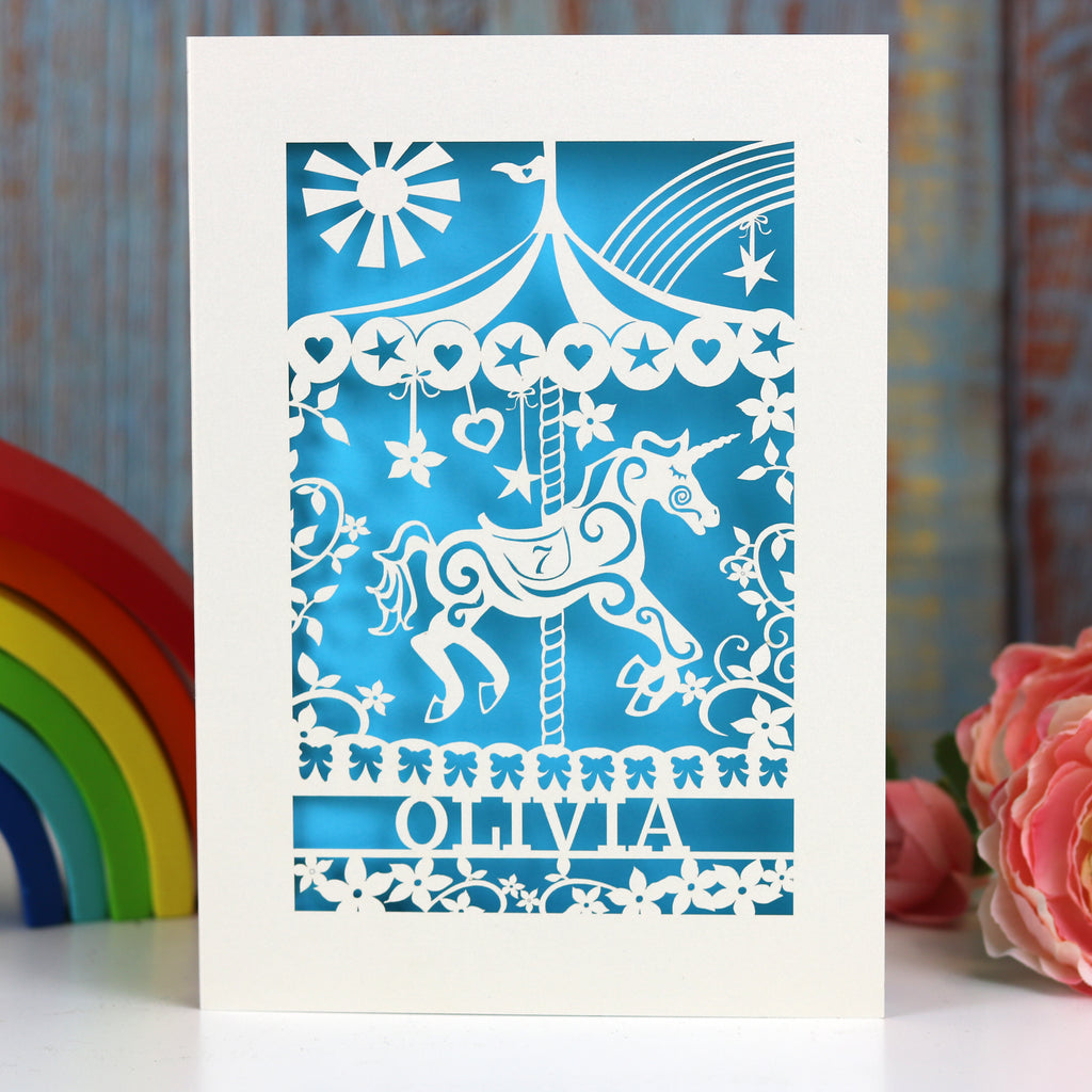 A super girly birthday card with a carousel unicorn and name and age. Laser cut card in cream with a blue paper insert.