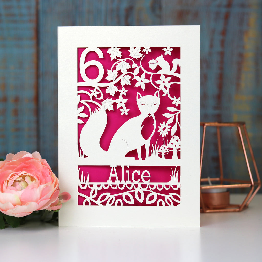 A personalised birthday card with a fox and a name. Card is cut away to reveal a shocking pink paper behind