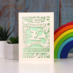 Gender neutral new baby personalised papercut card in cream with a light green insert. Shows Croeso i'r Byd , welcome to the world in Welsh, with a lovely laser cut scene showing a stork carrying a baby bundle surrounded with flowers and leaves. Space to put baby's name and date of birth under the stork.