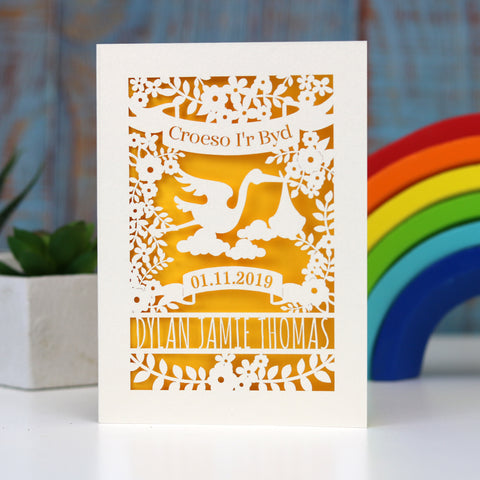 Welsh language Welcome to the World new baby papercut card. Has Croeso i'r Byd in a banner over a sweet stork bringing a baby. Flowers, leaves and space for the baby's name and date of birth. Shown here cut from cream card and finished with a  gender neutral sunshine yellow - A6 (small) / Sunshine Yellow
