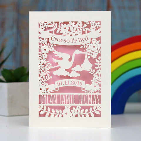 Pretty pink Croeso i'r Byd, Welsh Welcome to the world new baby papercut card.  Showing a stork, leaves and flowers with a banner for the date of birth and lines for the baby's name. Laser cut from cream card with a baby pink insert paper. - A6 (small) / Candy Pink