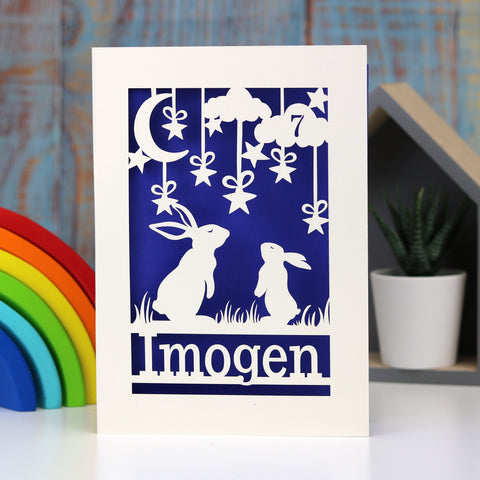 A personalised birthday card for a grandchild. Card is cream and has 2 rabbits looking at the moon in the sky. Background is purple, and the card is personalised with an age and name - A5 / Infra Violet