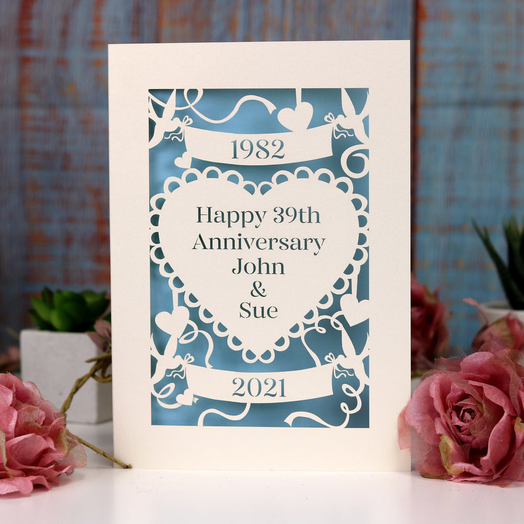 A paper cut wedding anniversary card. Card is cream, with laser cut details cut away to show a light blue paper behind. 