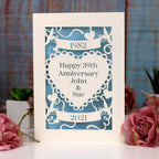 A paper cut wedding anniversary card. Card is cream, with laser cut details cut away to show a light blue paper behind. 