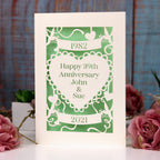 Personalised anniversary card, laser cut from cream with a light green paper behind. Design has a banner at the top with the year of the wedding, a heart in the centre with "Happy 39th anniversary John & Sue" and a banner underneath with the current year.