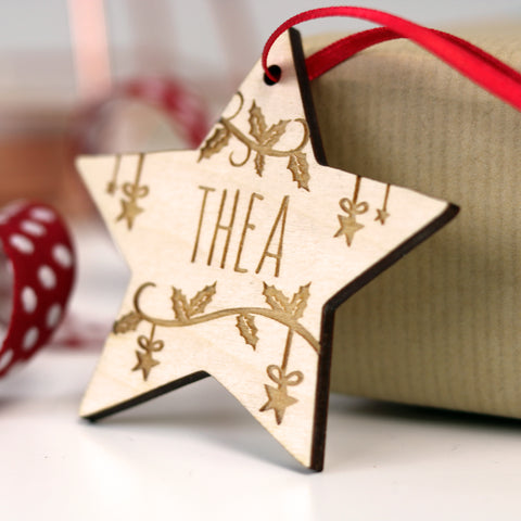 A personalised Christmas decoration in the shape of a star, engraved wood with a name and leaf design. - 