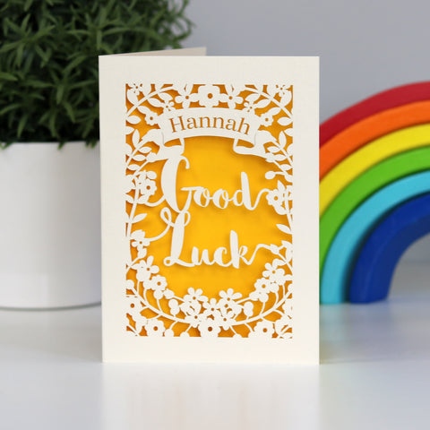 Sunshine yellow and cream laser cut Good Luck card. Shows the words "Good Luck" cut from cream card, with a banner above for the personalisation and surrounded with flowers.