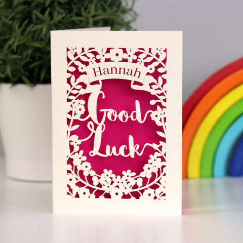 Striking papercut card in Cream with a bright pink background. Shows the words "Good Luck" surrounded by flowers and a name in the banner above. - A5 / Shocking Pink