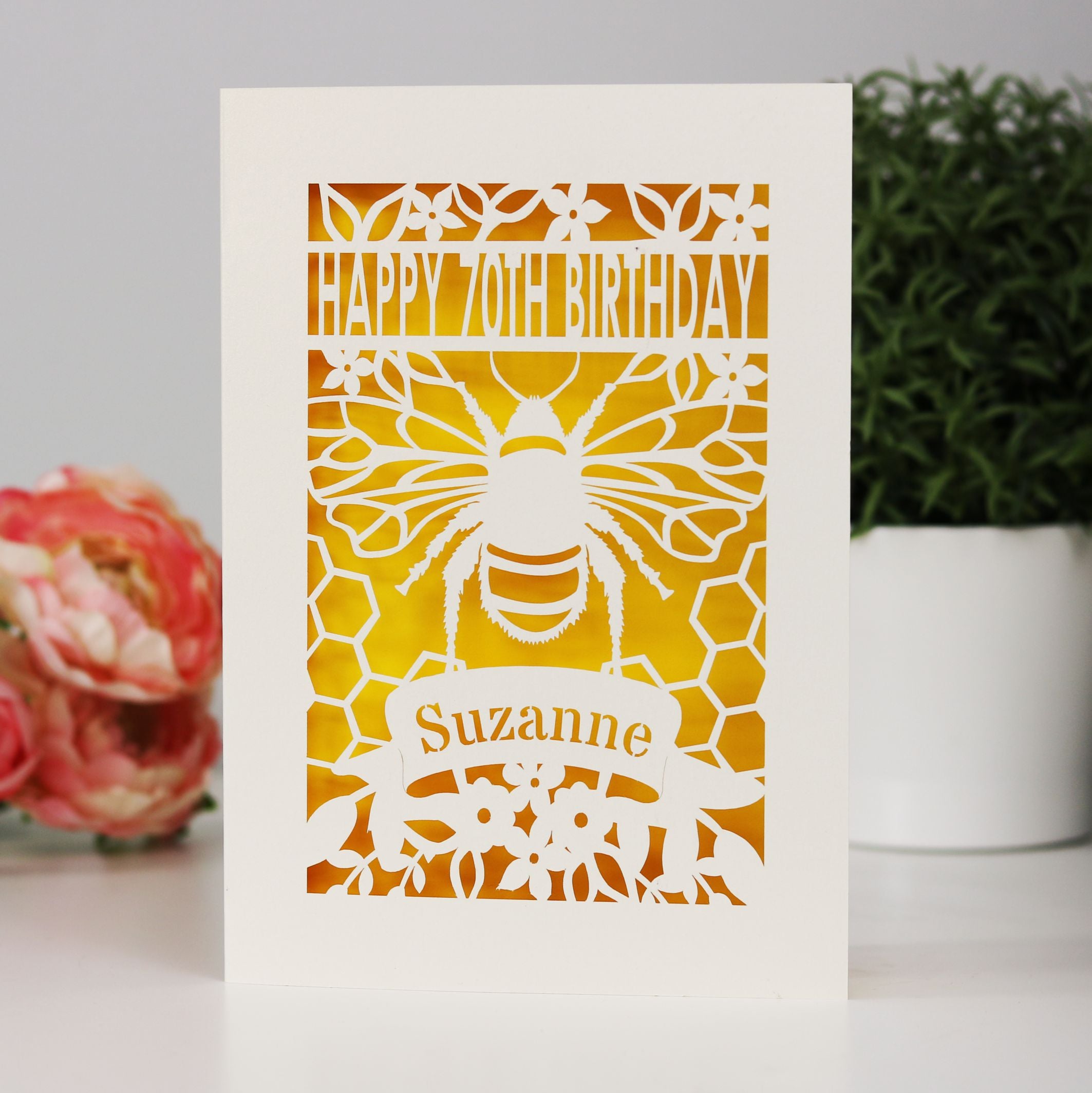 Lasercut personalised Bee design birthday card, shown as a Happy 70th Birthday and personalised with a name. Cut from cream card with a sunshine yellow background.