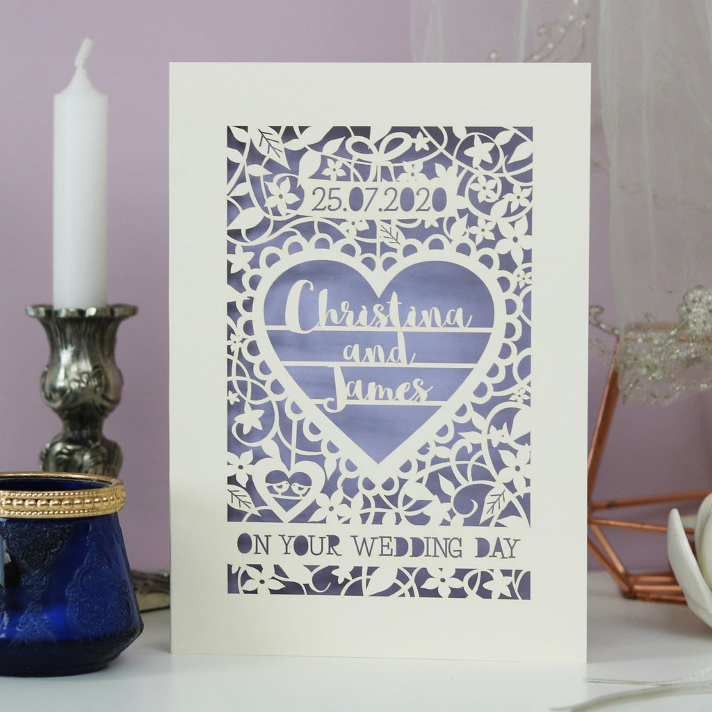 A personalised papercut wedding card featuring the date, the names "Christina and James" inside a heart and the words "On your wedding day" surrounded by floral details and two tiny birds inside a heart.