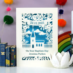 A paper cut card that reads "On Your Baptism Day" with a name underneath and a date in a banner above a cute little church. 