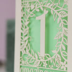  A close up image of a detail from a laser cut card. Cream card is cut away to reveal a light green paper insert behind. 