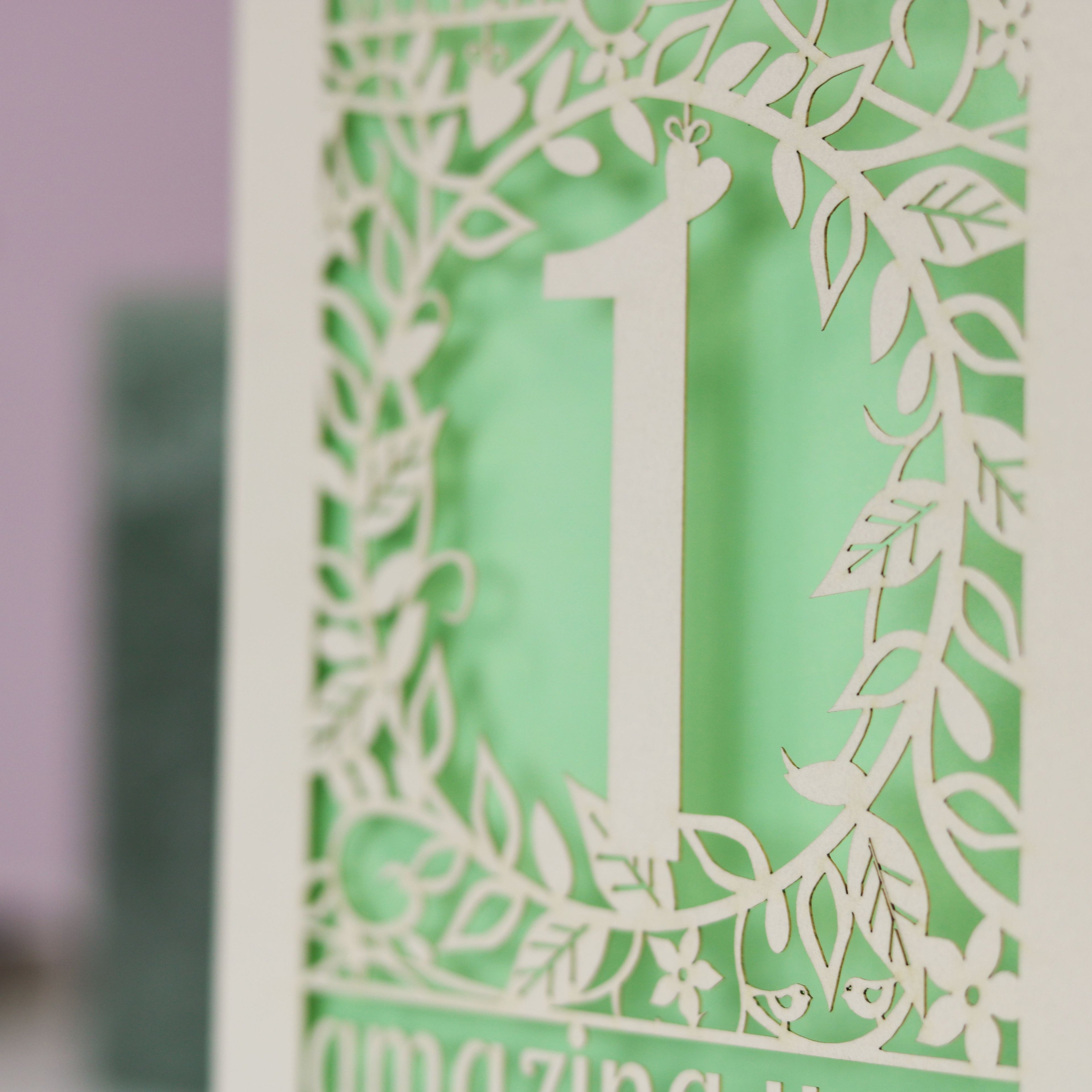  A close up image of a detail from a laser cut card. Cream card is cut away to reveal a light green paper insert behind. 