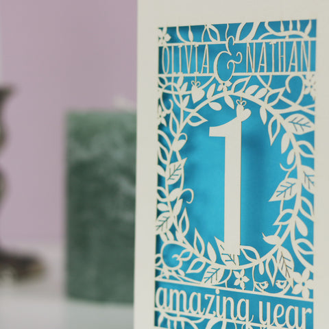 Personalised cards for wedding anniversaries. Image shows a laser cut first anniversary card with floral details and the words "Olivia & Nathan, 1 amazing year." - A5 / Peacock Blue